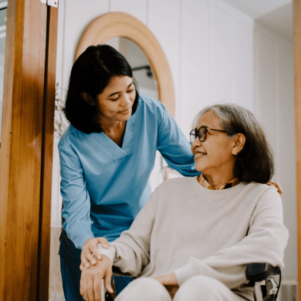 A caregiver in scrubs reviewing a discharge checklist with a patient seated comfortably in a home environment